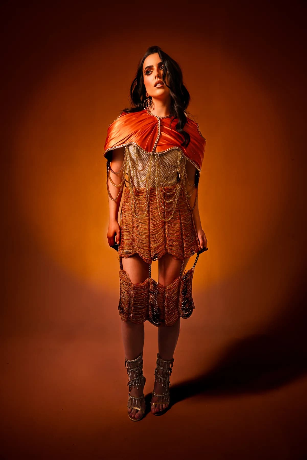 Model in an orange chain-draped garment against an amber studio background